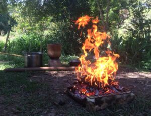 place in naurture with a fire in the foreground and tools in the background, burnig bark for Cacau ash
